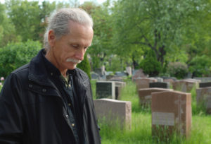 Sorrowful man standing in cemetery with head bowed