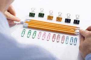 The camera looks over a man's shoulder as he arranges pencils to be exactly aligned.