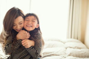 Parent and child hugging happily on bed, smiling at each other