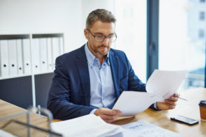 Professional sitting at desk reads through papers with serious expression