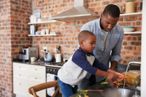 Father and child wash vegetables at sink in small, bright kitchen