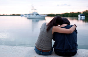 Rear view of two women sitting on pier embracing. 