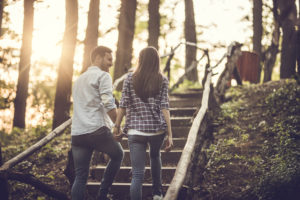 Rear view of couple talking as they hold hands and climb stairs along forest trail