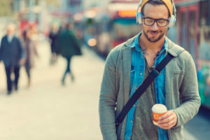 Person walks down the street with headphones on, holding coffee, smiling calmly