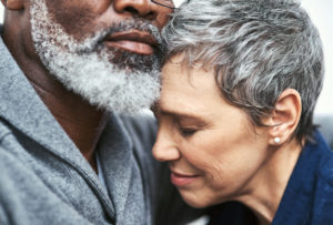 A close up of a woman smiling as she leans into her husband's shoulder.