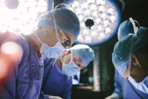 A team of surgeons concentrate on their work as bright lights shine in the background.