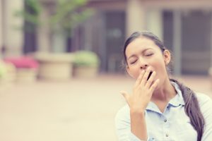 Woman yawns and covers mouth outside.