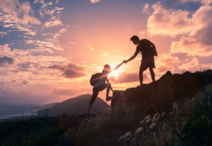 Hikers help each other up mountain under setting sun