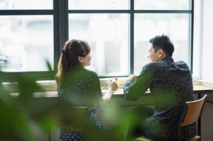 Adult couple sit at window table in cafe, facing each other and talking