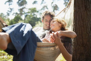 A happy couple sits cuddling in hammock in the afternoon