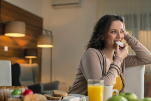 Person with long curly hair sits at table eating bagel and drinking juice