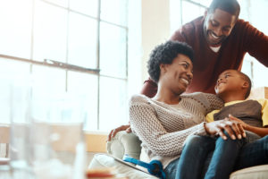 Parents and young child sit together on sofa in living room smiling happily