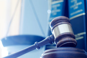 A gavel sits in front of books and a scale. The photo has a strong blue filter.