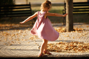 Child in pink dress dances outside among autumn leaves