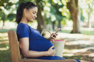 Pregnant woman texting with cell phone on park bench