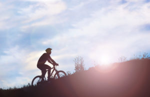 Person on bike with helmet rides uphill against blue cloudy sky