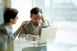 Two adults sitting at table with laptop looking sadly down together