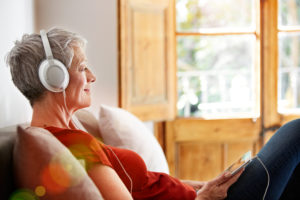 A mature woman smiles as she listens to a song through her headphones.