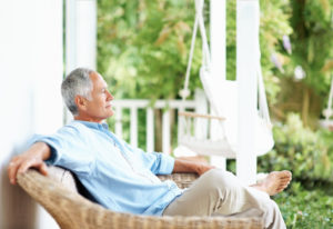 Relaxed older adult with short gray hair sits on porch, leaning back, with eyes closed
