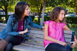 Teen listens to music with headphones, turned away from her mother, who is trying to talk to her