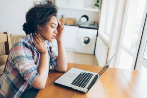 Person sits at table with laptop, looking distracted by pain in head