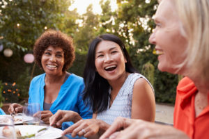 Three friends sit outside talking and laughing while eating in late afternoon