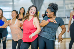 Two adult friends playfully bump their hips together in dance class.