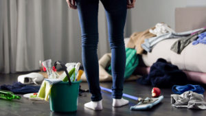 Person looks down at mess in room with bucket of cleaning supplies, ready to clean up