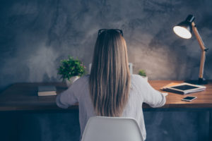 Back view of woman sitting at neatly arranged desk in lamplight