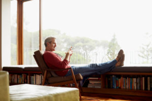 Side view of older adult relaxing with feet up, looking out large window