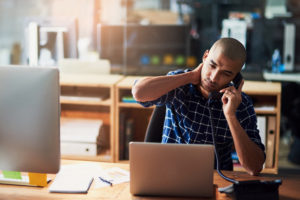 Person wearing buttoned shirt with shaved head talks on phone with stressed, tired expression