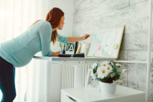 Pregnant adult with long hair leans over table and works on organizing vision board 