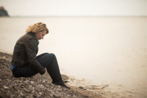 Thoughtful person sits on rock by lake