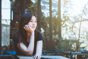 Woman sits at table in outside cafe, looking thoughtful