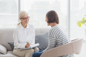 Therapist sits on couch across from person in therapy, smiling and talking.