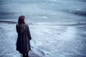 A woman stands alone on a frozen lake.