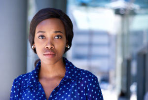 A woman in a blue shirt stares at the camera without any facial expression.