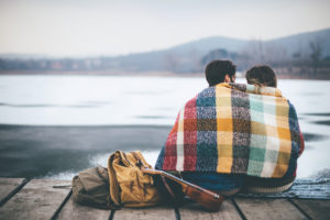 Couple wrapped in blanket sits looking out over lake