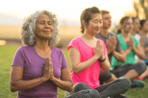 A senior woman sits outdoors in a meditation group.