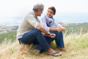 Mature adult couple sit on rock talking openly and smiling