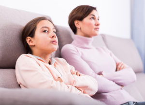 Mother and daughter sit on couch, not acknowledging each other after argument.