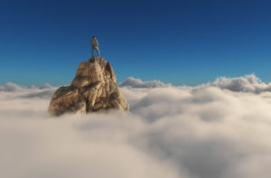 Man stands on pointed, rocky cliff that juts out above a layer of clouds.