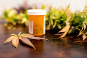 Pot leaf on wooden table next to prescription bottle