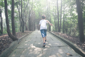 Rear view photo of older child running down stone path into forest