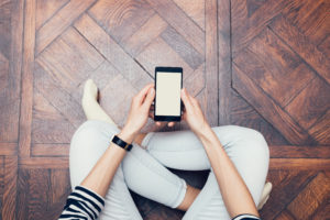 Overhead view of person sitting on wood floor holding a smartphone