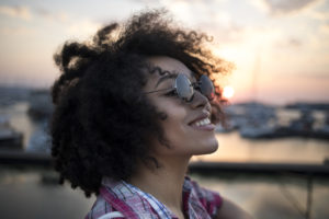 Young adult with natural hair smiles and looks up outside at sunset