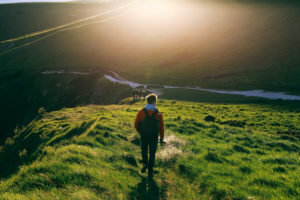 Rear view of person walking to meet others on grassy hill on bright day