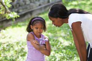 A mother crouches down to talk to her upset preschool-age daughter.