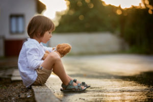 Child sitting on step with stuffed toy at sunset