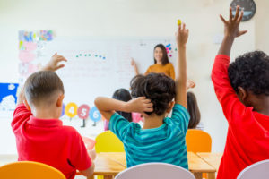 Three young boys raise their hands to answer a teacher's question.